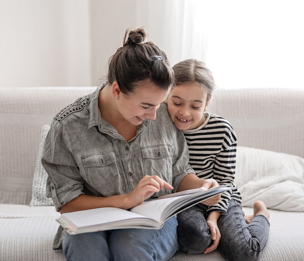Fröhliche Mutter und Tochter ruhen sich zu Hause aus und lesen gemeinsam ein Buch