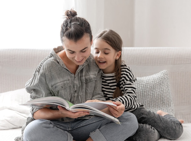 Fröhliche Mutter und Tochter ruhen sich zu Hause aus und lesen gemeinsam ein Buch