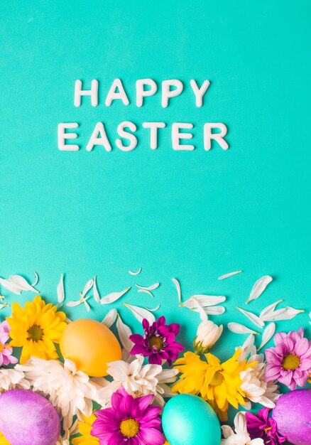 Fröhliche Ostern-Wörter nahe hellen Eiern und den Blumenknospen