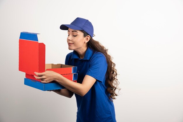 Fröhliche Pizzabote in blauer Uniform schnüffelt an einer Schachtel. Foto in hoher Qualität