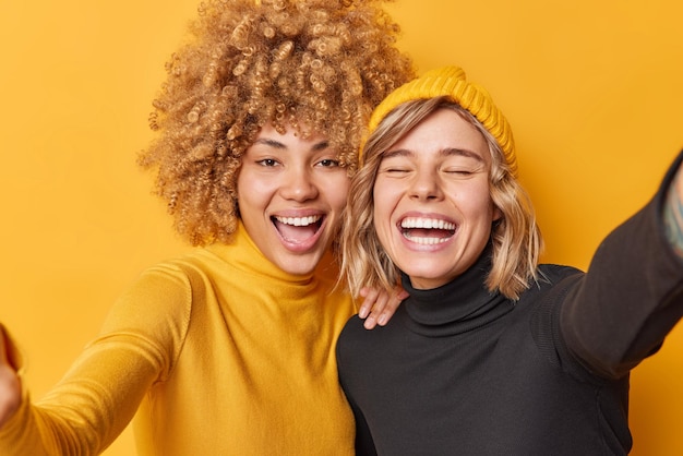 Fröhliche positive junge Frauen haben Spaß lachen gerne Selfie in Freizeitkleidung gekleidet stehen nebeneinander isoliert auf gelbem Hintergrund Fröhliche Freundinnen fotografieren sich