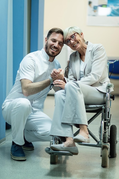 Kostenloses Foto fröhliche reife frau im rollstuhl, die mit ihrem arzt im krankenhausflur händchen hält