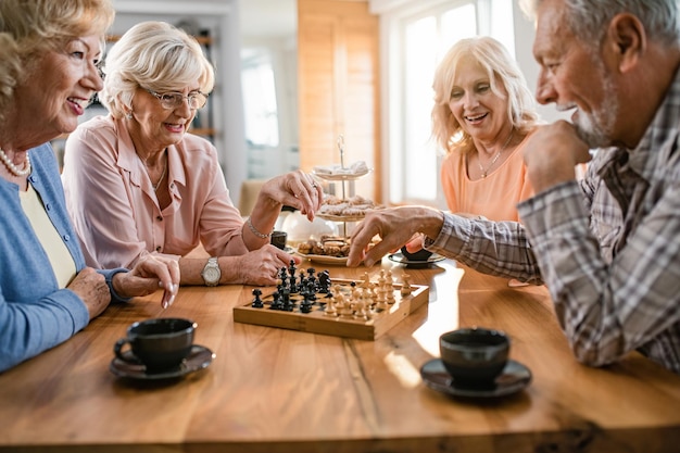 Fröhliche reife Freunde, die sich beim Schachspielen während der Kaffeezeit zu Hause amüsieren