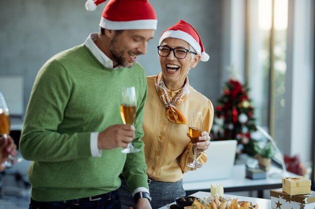 Fröhliche, reife Geschäftsfrau, die Champagner trinkt und mit einem Kollegen auf der Neujahrsparty spricht