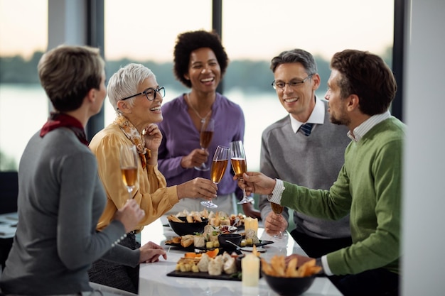 Fröhliche reife Geschäftsfrau und ihre Kollegin stoßen auf einer Büroparty mit Champagner an