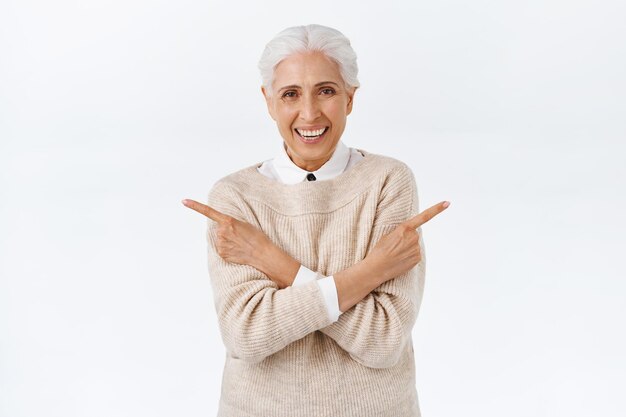 Fröhliche, schöne ältere Frau mit grauem gekämmtem Haar, schicke elegante Kleidung tragen, die Hände mit verschränkten Armen über der Brust seitlich zeigen, lächeln und lachen