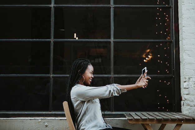 Fröhliche schwarze frau macht ein selfie in einem straßencafé
