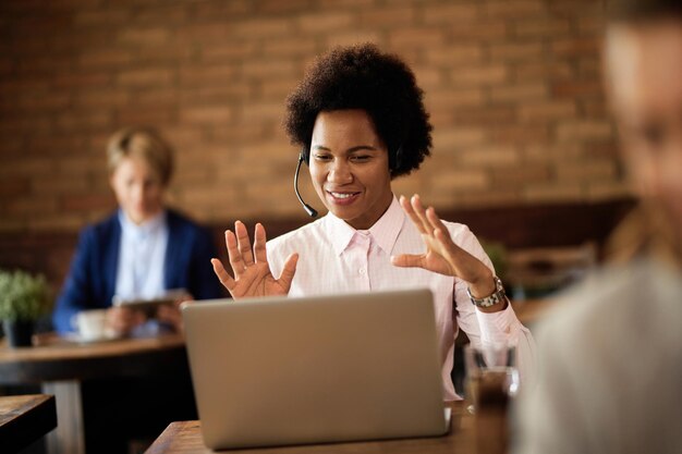Fröhliche schwarze Geschäftsfrau, die in einem Café einen Videoanruf über einen Laptop tätigt