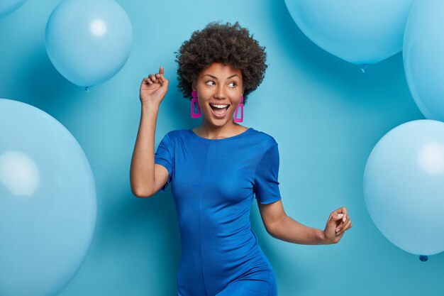 fröhliche sorglose Frau tanzt und hat Spaß in modischen Kleidern hat festliche Stimmungsposen gegen blaue Luftballons