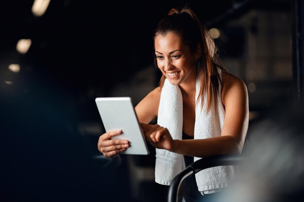 Fröhliche Sportlerin, die ihren Trainingsplan auf einem digitalen Tablet erstellt, während sie im Fitnesscenter Sport trainiert