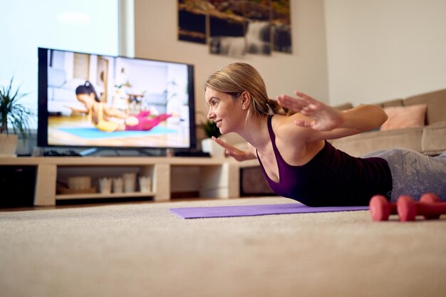 Fröhliche Sportlerin stärkt ihren Rücken in Locust-Pose beim Heimtraining