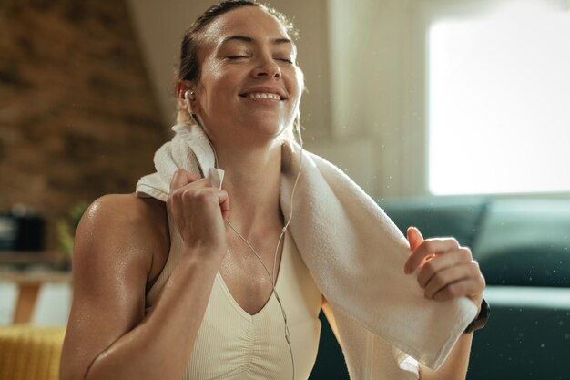 Fröhliche Sportlerin wischt sich den Schweiß ab, während sie eine Pause macht und Musik über Kopfhörer hört.