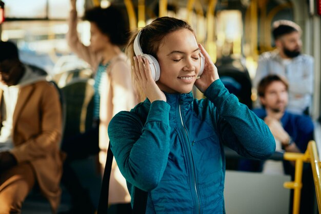 Fröhliche sportliche Frau, die Musik mit geschlossenen Augen in öffentlichen Verkehrsmitteln hört