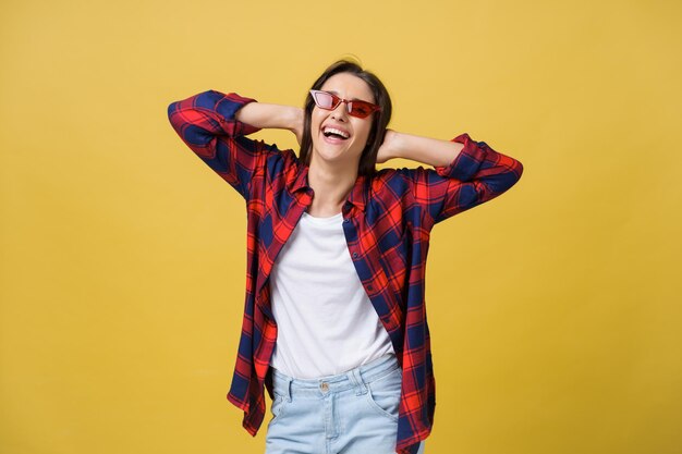 Fröhliche, stilvolle, moderne Frau mit modern geformter Sonnenbrille, die lachend auf Ihre Kamera schaut, die auf gelbem Hintergrund isoliert ist Glückskonzept