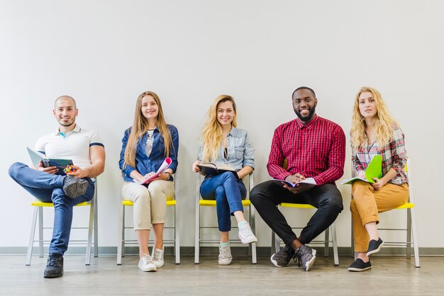 Fröhliche Studenten posieren auf Stühlen