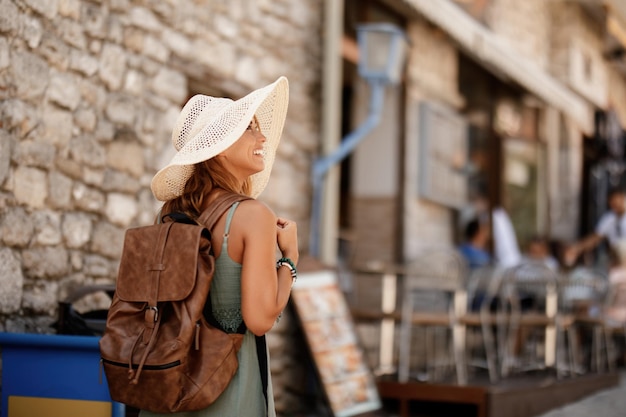 Fröhliche weibliche Touristin mit Rücken, die einen Spaziergang macht und die Stadt im Sommerurlaub erkundet