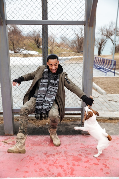 Fröhlicher afrikanischer Mann, der mit Hund spielt und draußen lacht