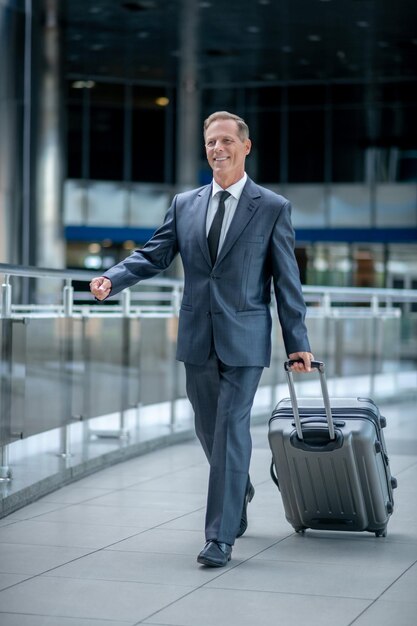 Fröhlicher Geschäftsmann, der sein Gepäck durch das Flughafenterminal rollt