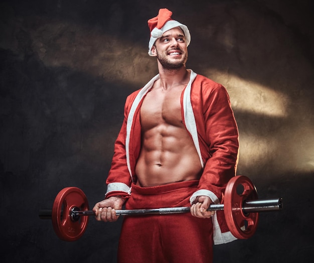 Fröhlicher gutaussehender Mann posiert für Fotografen im Weihnachtskostüm, während er Langhantel hält.