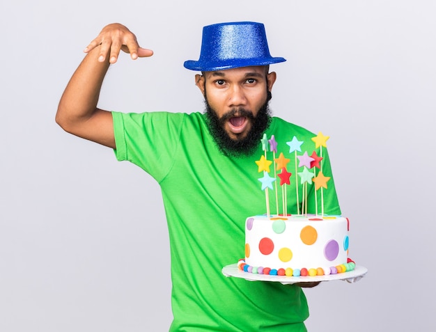 Fröhlicher junger afroamerikanischer kerl mit partyhut, der kuchen hält, der die hand hebt