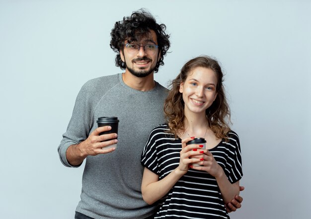 Fröhlicher junger Paarmann und Frau, die Kameras betrachten, die mit glücklichen Gesichtern lächeln, während Handys stehen, die über weißem Hintergrund stehen