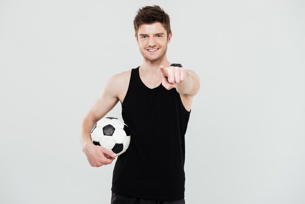 fröhlicher junger Sportler mit Fußball, der lokal über weißem Hintergrund steht. Blick auf die Kamera.