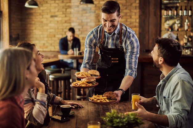 Fröhlicher Kellner, der einer Gruppe fröhlicher Freunde in einem Pub Essen serviert