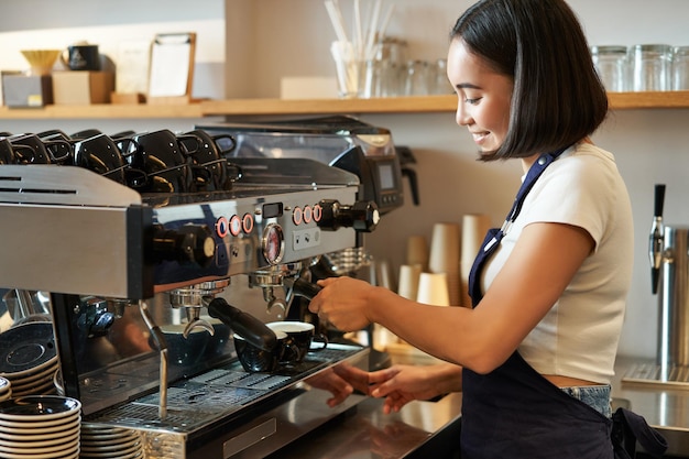 Fröhlicher lächelnder Barkeeper Barista mit Kaffeemaschine bereiten Bestellungen vor, die Cappuccino oder Latte Wearin machen