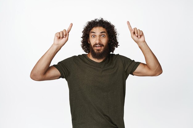 Fröhlicher lächelnder Mann, der mit dem Finger nach oben zeigt und das Werbeangebot-Verkaufsbanner nach oben zeigt, das im T-Shirt auf weißem Hintergrund steht