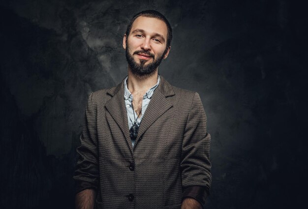 Fröhlicher lächelnder Mann mit Amulett am Hals posiert für Fotografen im dunklen Fotostudio.