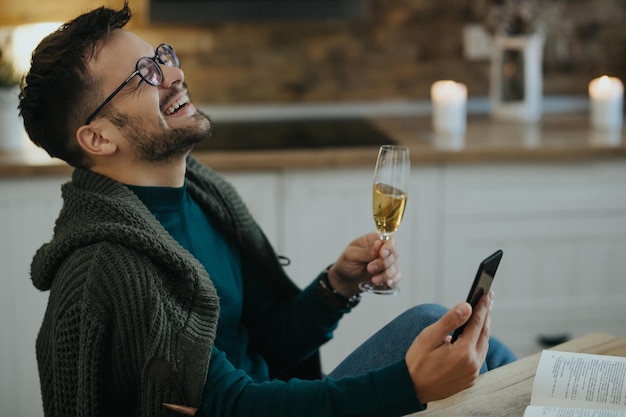 Fröhlicher Mann, der Champagner trinkt, während er zu Hause ein virtuelles Date über das Smartphone hat