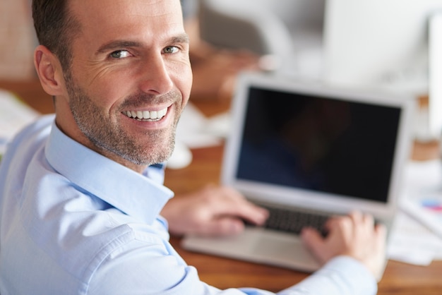 Kostenloses Foto fröhlicher mann, der sich dreht und lächelt, während er am computer arbeitet