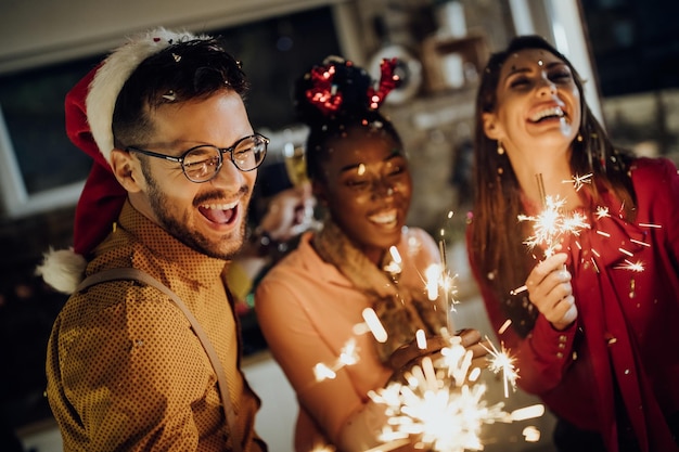 Fröhlicher Mann und seine Freunde amüsieren sich an Silvester zu Hause mit Wunderkerzen