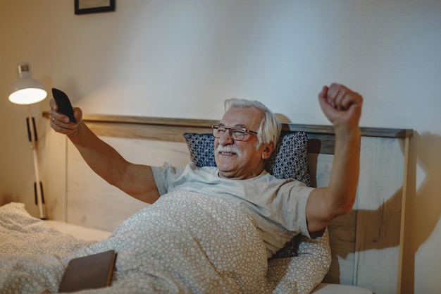 Fröhlicher reifer Mann jubelt, während er im Schlafzimmer Sportspiele im Fernsehen anschaut