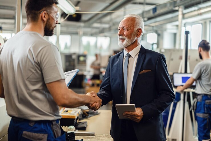 Kostenlose Foto fröhlicher, reifer unternehmensleiter, der mit einem arbeiter beim besuch der fabrikanlage hände schüttelt