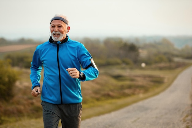 Fröhlicher Senior-Sportler, der sich motiviert fühlt, während er Musik hört und in der Natur läuft Kopierraum