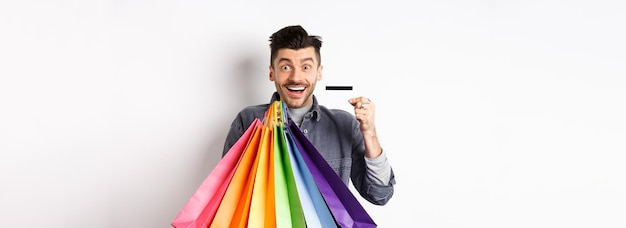 Fröhlicher Shopaholic mit bunten Einkaufstüten und lächelnder Plastikkreditkarte