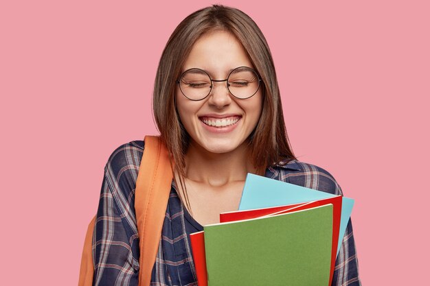 Fröhlicher Student, der mit Brille gegen die rosa Wand aufwirft