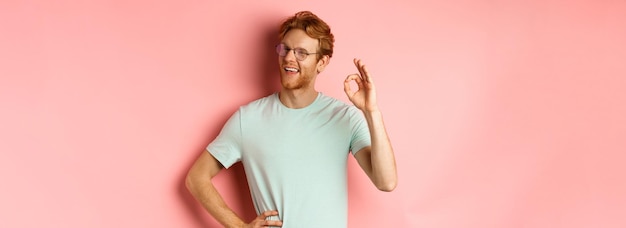 Kostenloses Foto fröhlicher typ mit roten haaren und bart, der eine brille trägt, die die zustimmung zeigt und lächelnd blinzelt