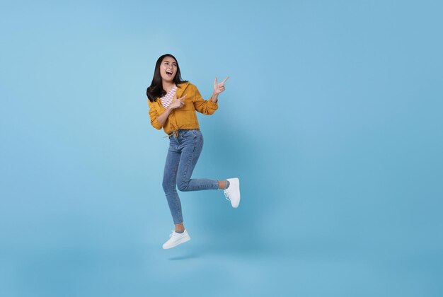 Fröhliches asiatisches Mädchen, das mit dem Zeigefinger in die Luft springt, um den Raum zu kopieren, mit lächelndem Gesicht und glücklich