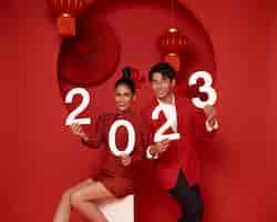 Kostenloses Foto fröhliches asiatisches paar in roter freizeitkleidung mit der nummer 2023, das ein frohes neues jahr begrüßt