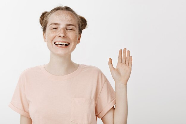 Fröhliches freundliches junges Mädchen, das gegen die weiße Wand aufwirft