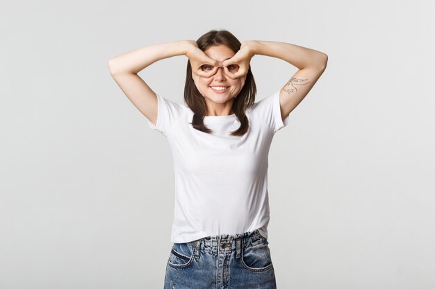 Fröhliches gutaussehendes junges Mädchen, das Superheldenmaske mit den Händen über den Augen macht und glücklich lächelt.