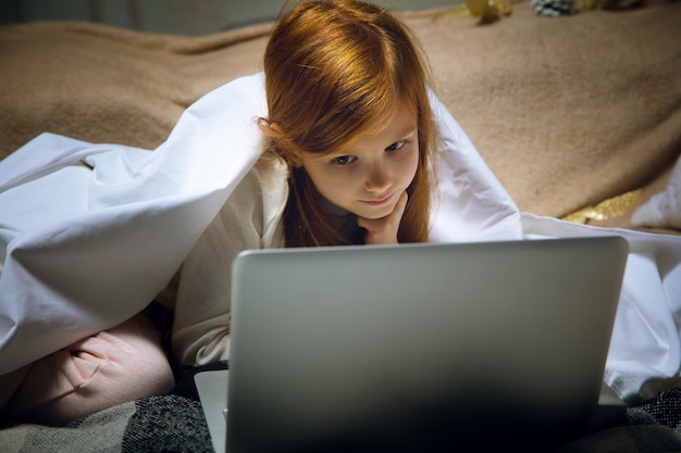 Fröhliches kaukasisches kleines Mädchen während Videoanrufen oder Nachrichten mit dem Weihnachtsmann mit Laptop und Heimgeräten