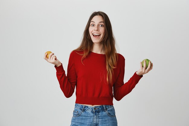 Fröhliches Mädchen, das Früchte zeigt, Äpfel mit beiden Händen hält und lächelt