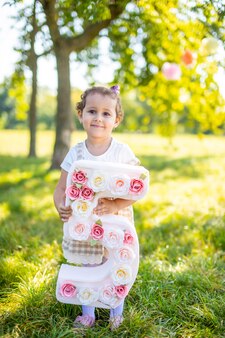 Fröhliches mädchen, das spaß am kindergeburtstag auf einer decke mit papierdekorationen im park hat