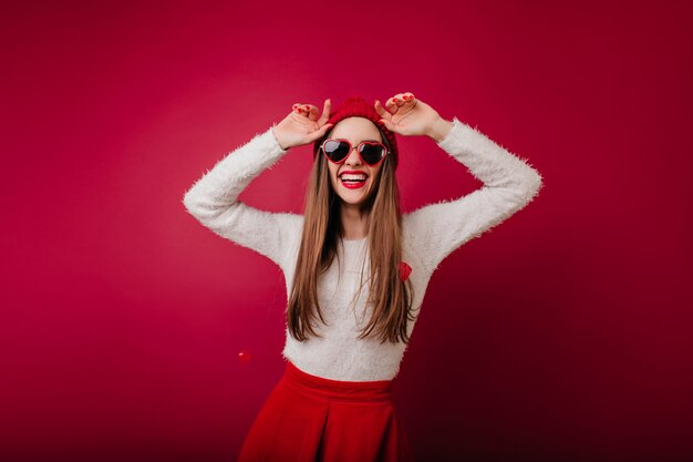 Fröhliches Mädchen im flauschigen Pullover, der im Rotweinraum tanzt