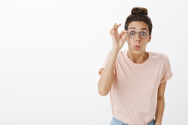 Fröhliches Mädchen mit Brille, die gegen die weiße Wand aufwirft