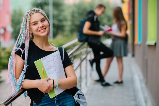 Fröhliches Mädchen mit Studien posiert draußen