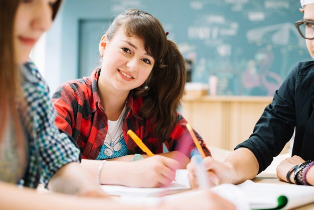 Fröhliches Mädchen sitzt mit Klassenkameraden am Tisch